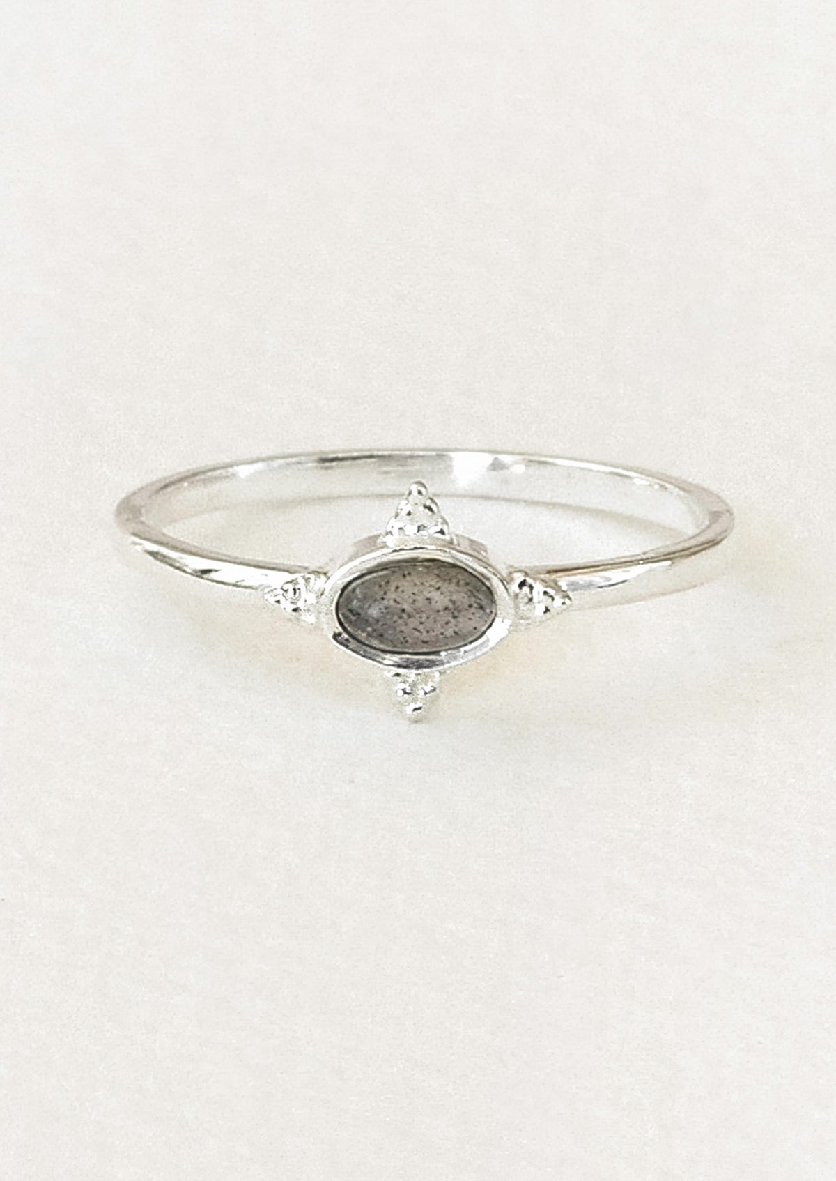 A sterling silver ring with a dark grey oval labradorite stone framed in a star shaped setting on a white paper.