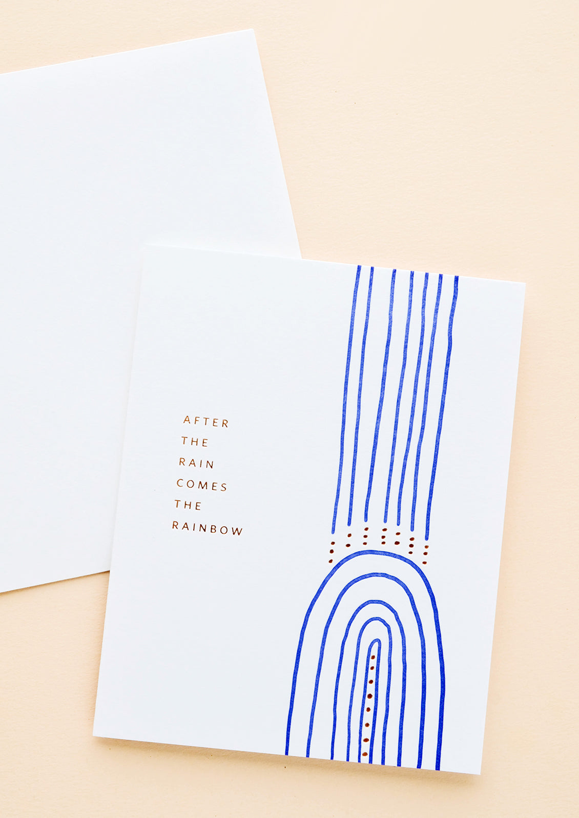 White greeting card with cobalt blue rainbow and gold text reading "After the rain comes the rainbow"