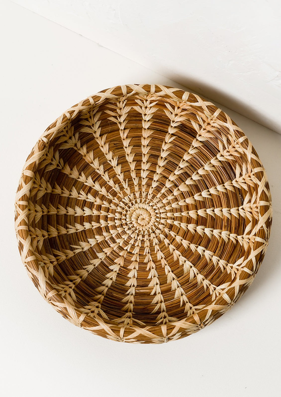 A shallow, round basket with lighter woven pattern throughout.