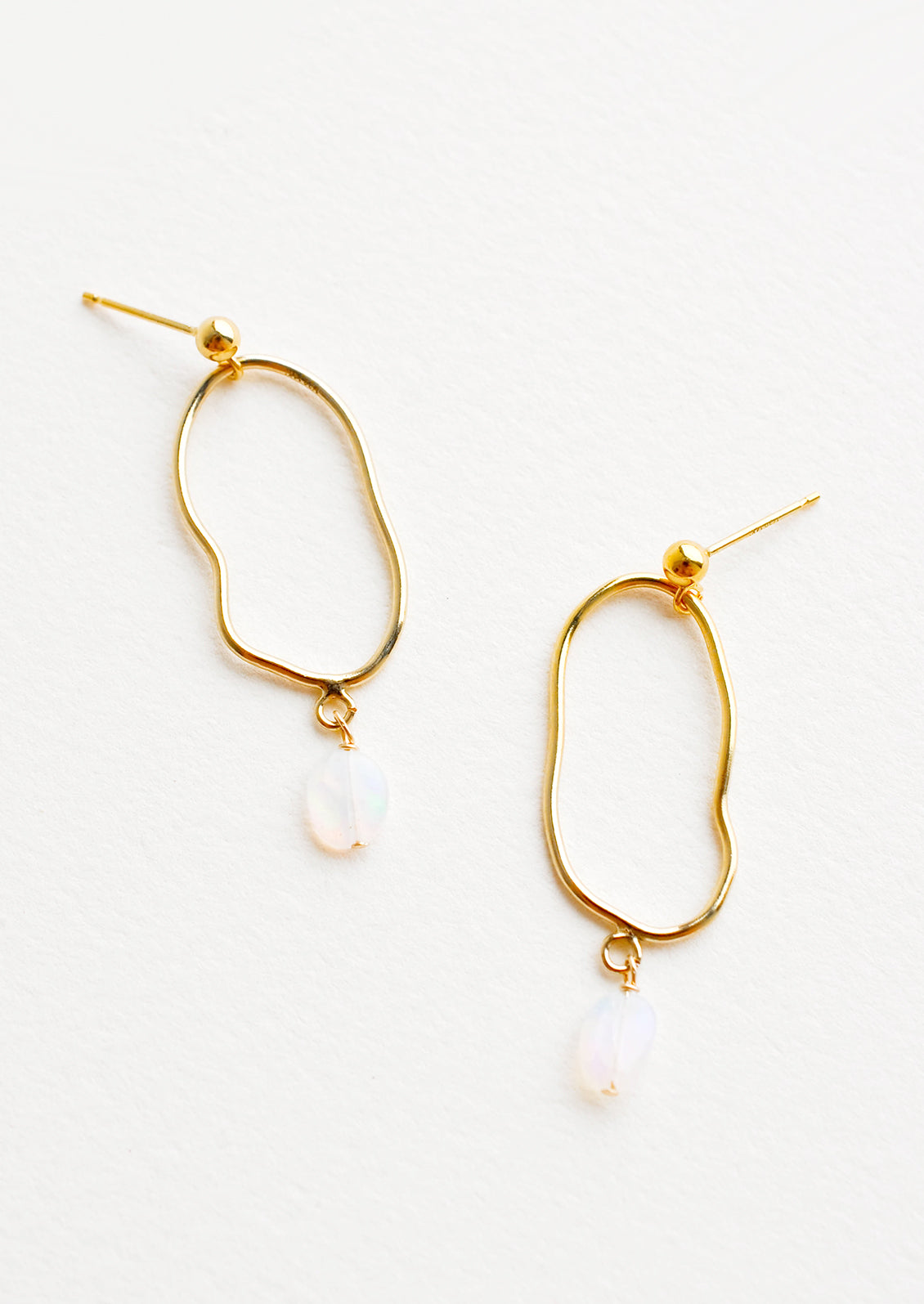Gold imperfectly shaped oval earrings each with a small dangling opal gemstone.
