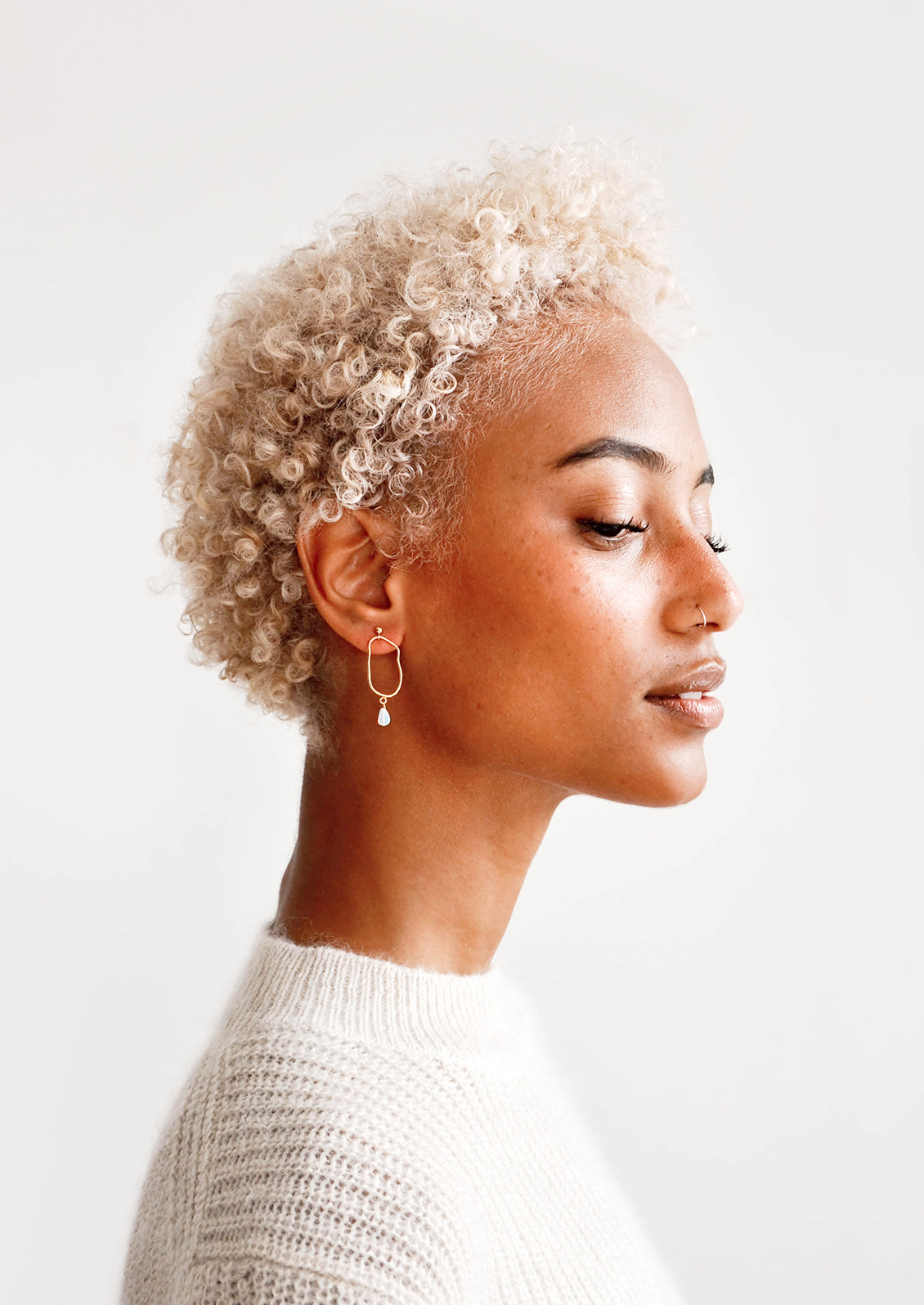 Model wears delicate gold and opal drop earrings and white sweater.