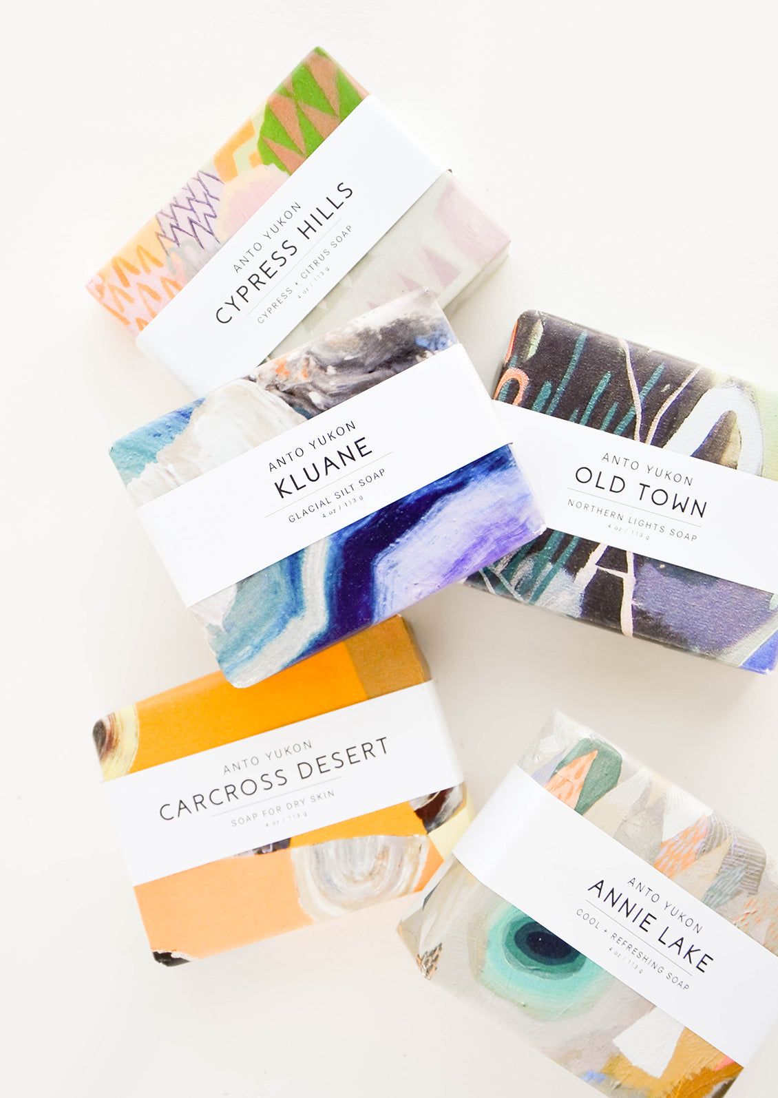 Five bars of soap in multicolored packaging with white labels.