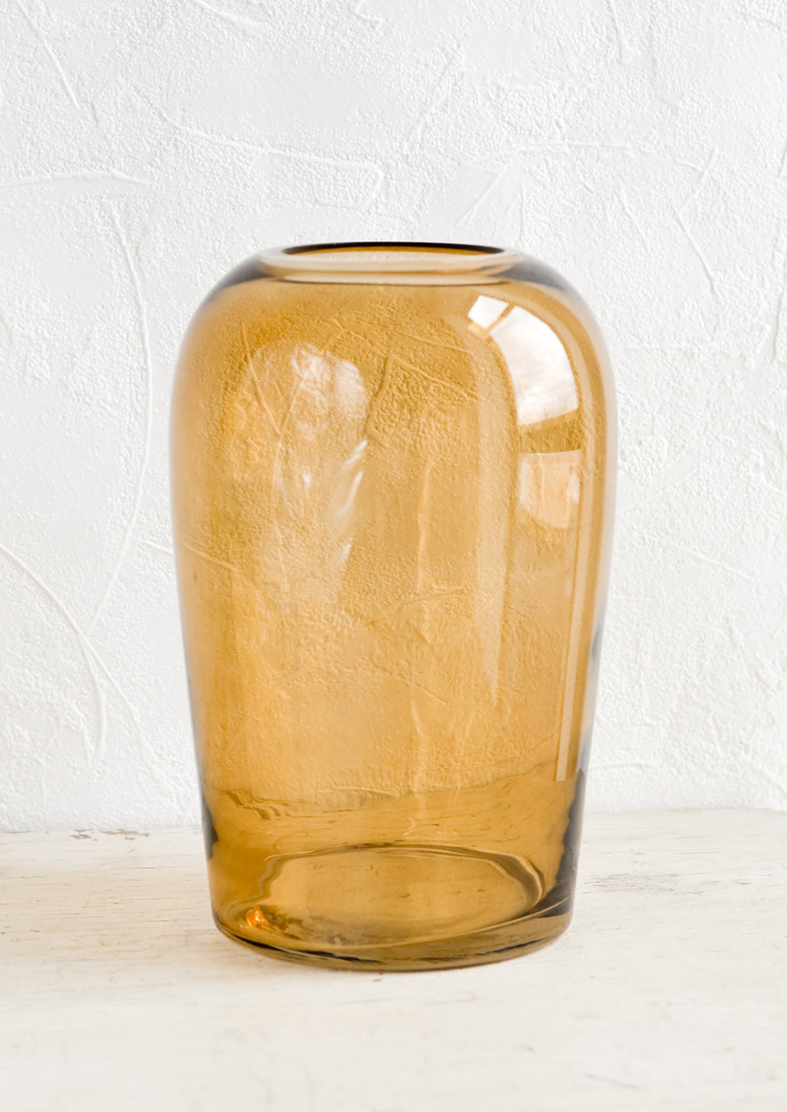 An empty glass vase in tall shape and amber brown color.