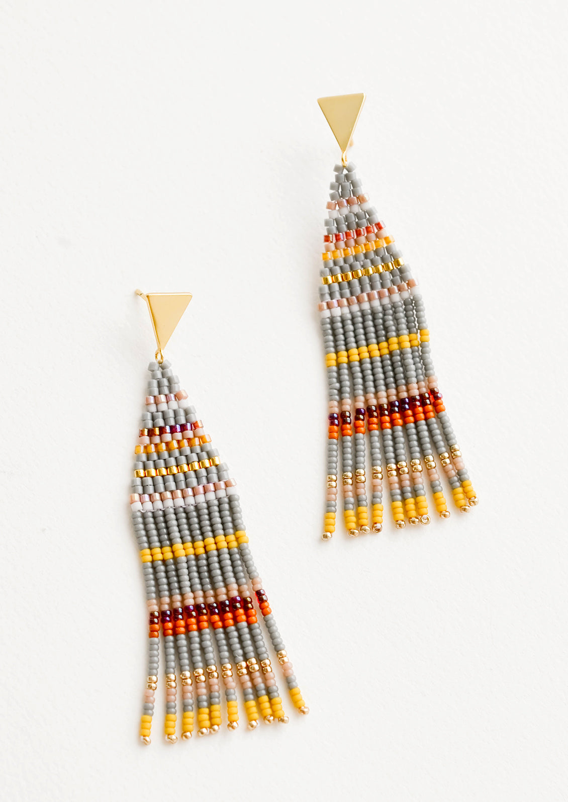 Fringe beaded earrings in gray with yellow, orange, gold, and maroon horizontal stripes on a triangular gold post.