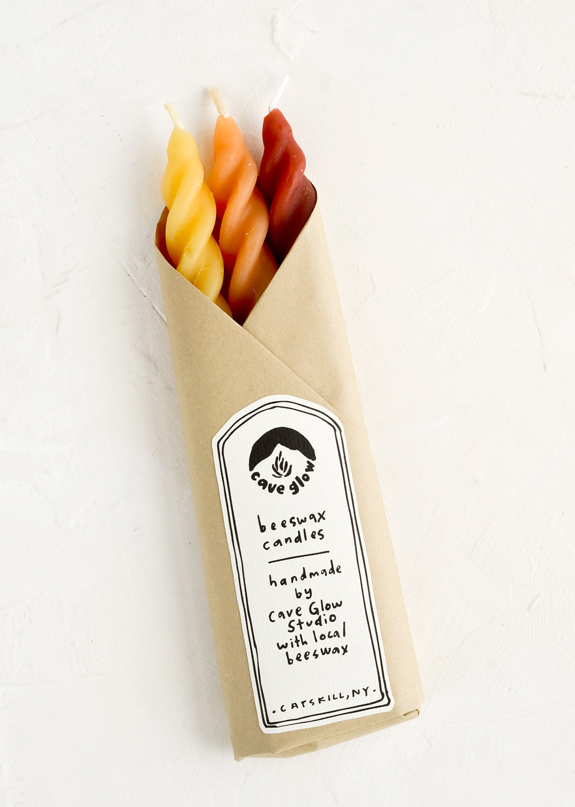 Three spiral beeswax tapers in orange, red and yellow wrapped in kraft paper.