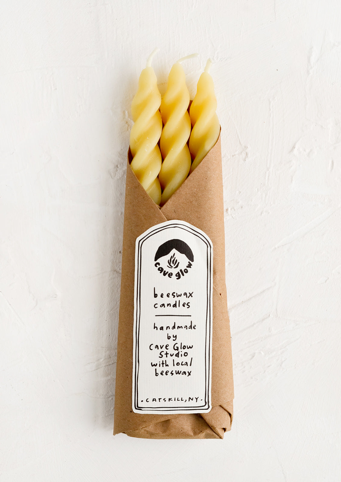 Three spiral beeswax tapers wrapped in kraft paper.
