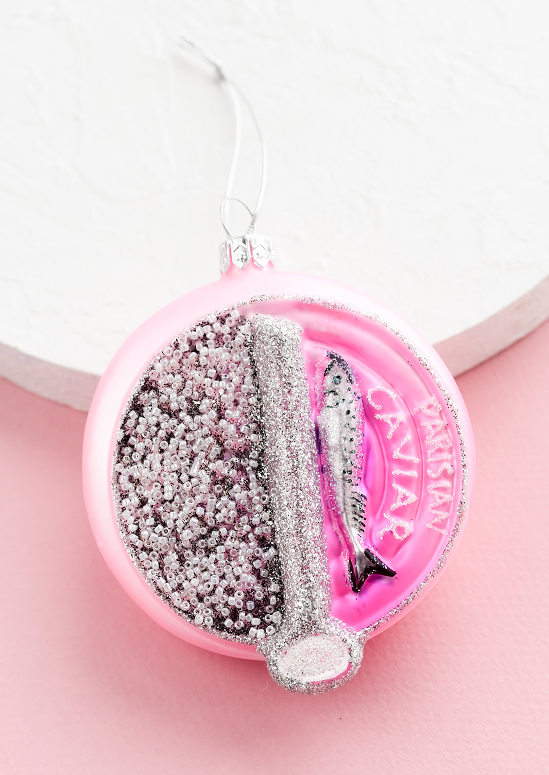 A glass ornament in the shape of round Parisian caviar tin.