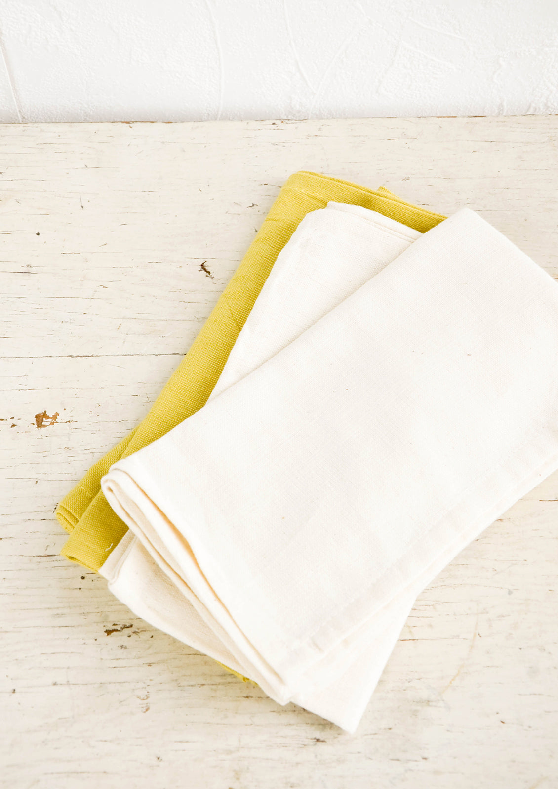 Folded cotton napkins in natural and chartreuse on a rustic table