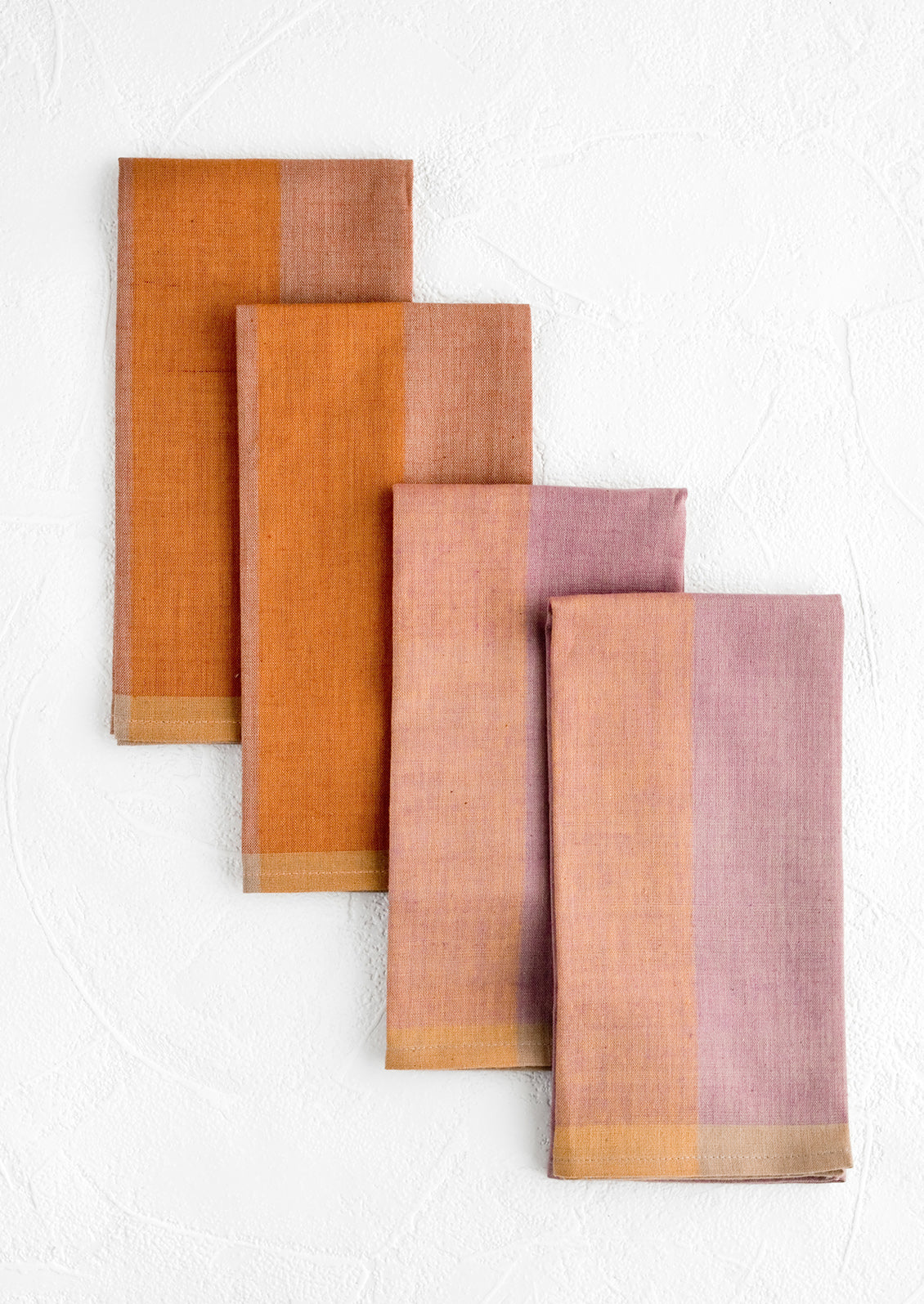 Four fabric napkins in purple and orange colorblock design.