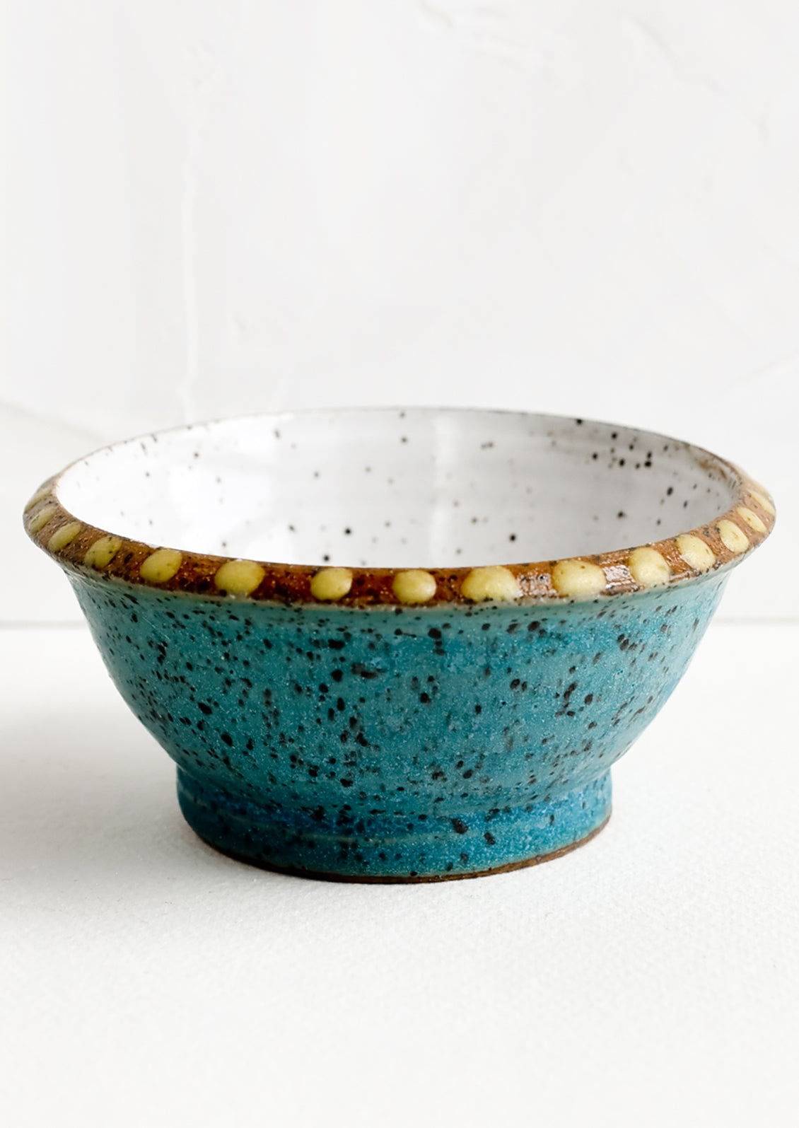 A small turquoise ceramic bowl with yellow dot painted detailing.