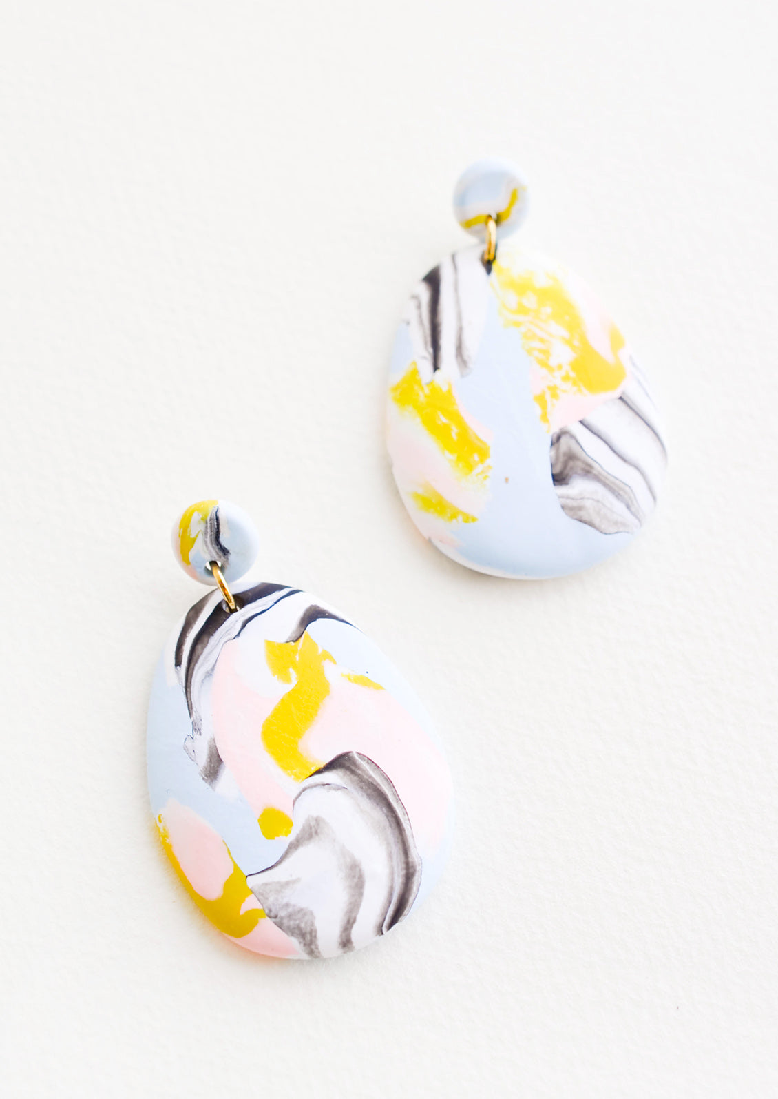 Blue, pink, yellow, and black marbled clay earrings, with a larger oval dangling from a small circle.