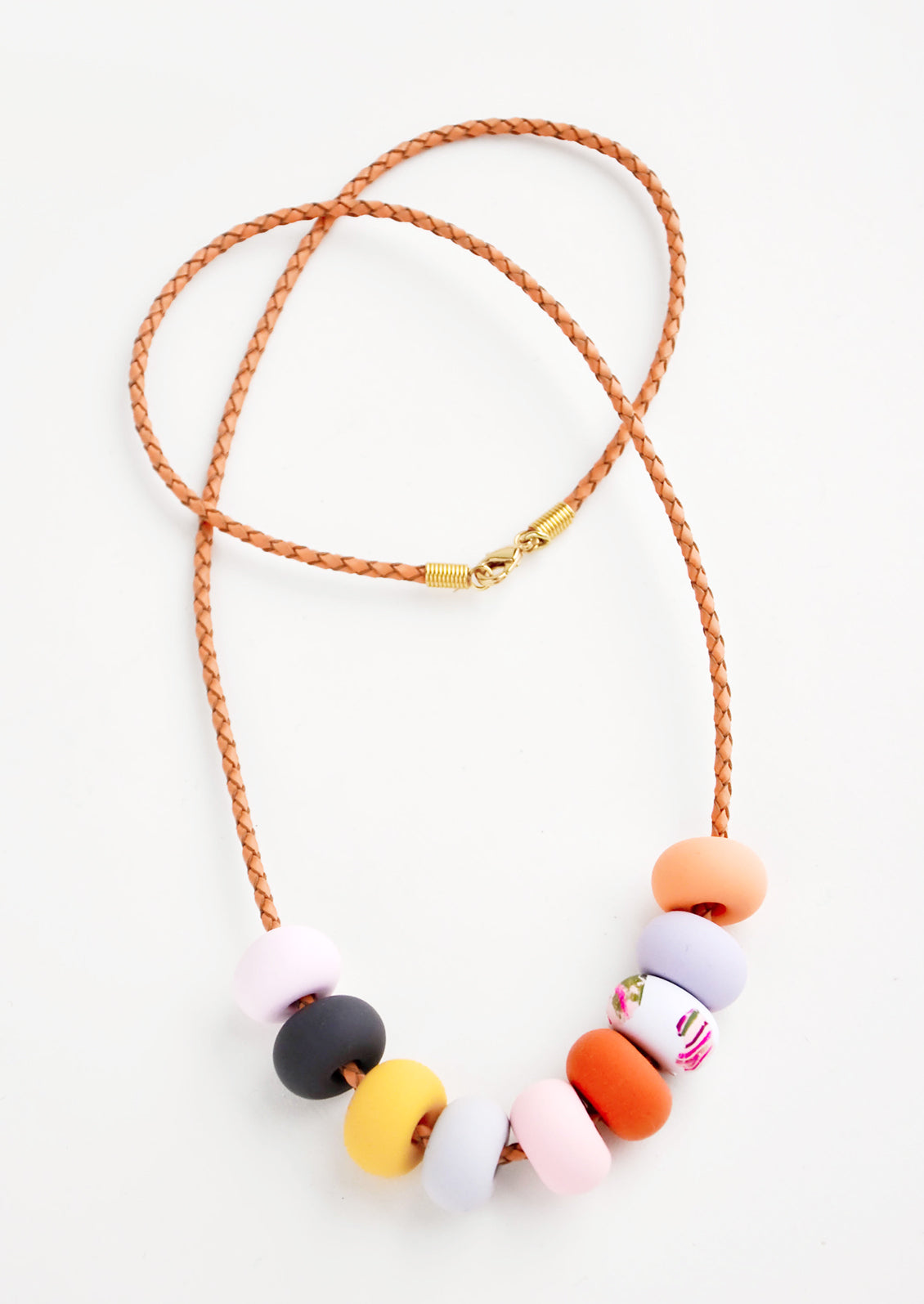 Necklace with light brown woven leather cord and nine clay beads in pink, navy, yellow, red, and orange.