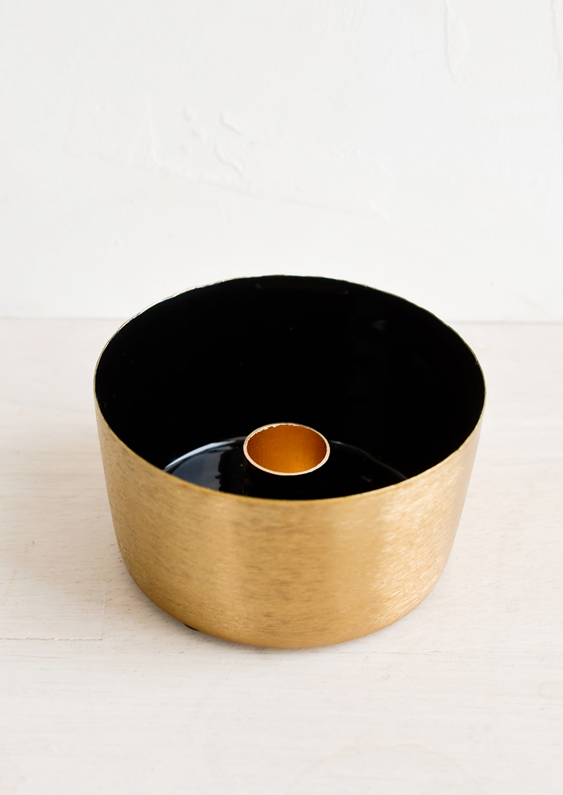 A round brass taper holder with high walls and black enamel lining.
