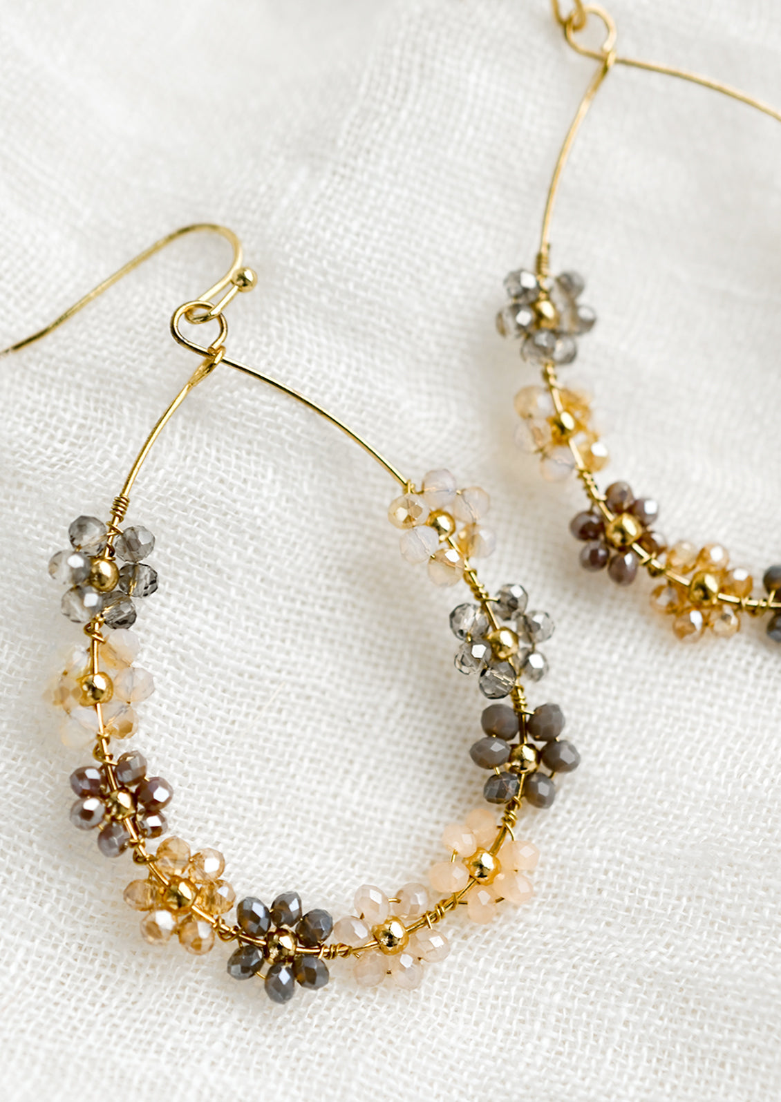 A pair of gold teardrop wire earrings with pastel floral beading.