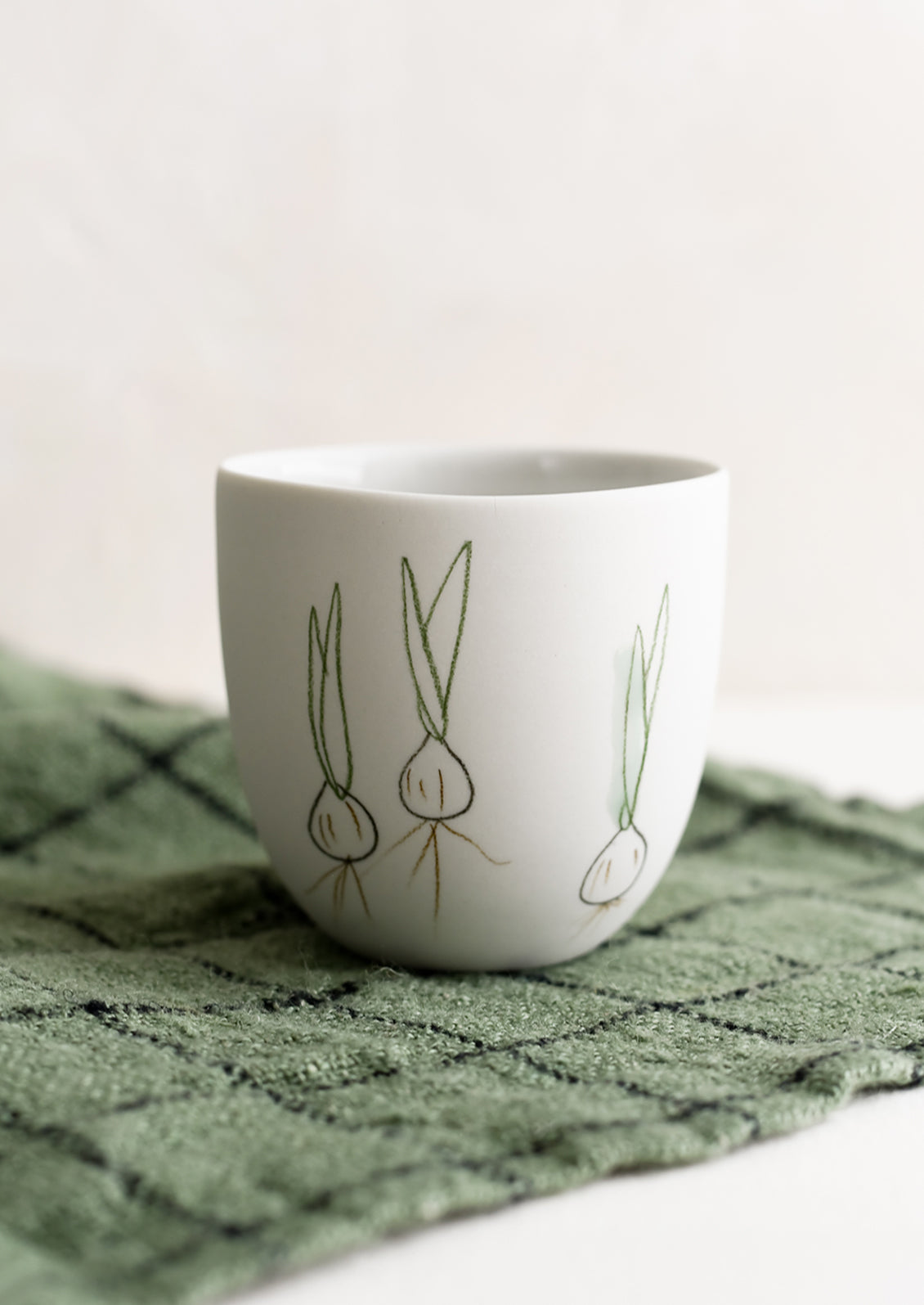 A small porcelain cup with hand drawn spring onions.