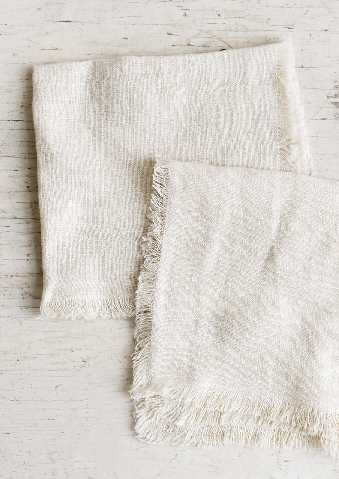 Folded cream colored linen napkins with frayed edges.