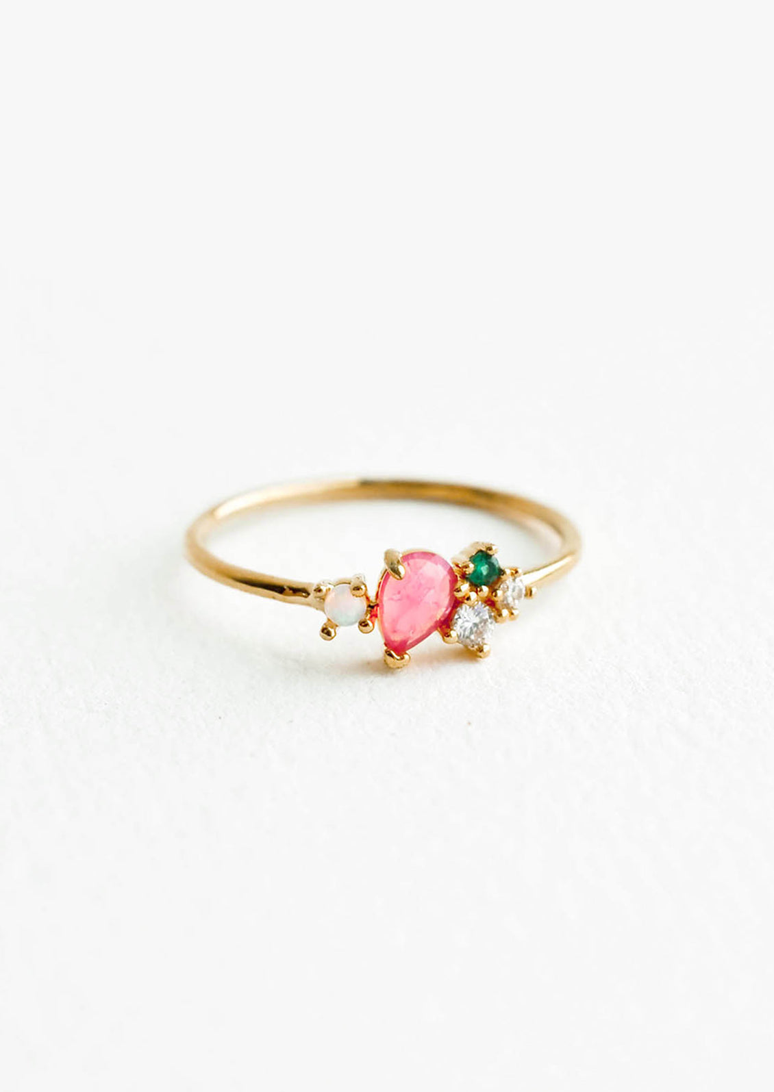 Gold ring featuring slim band with two gemstones and two crystals in pink, green and white hues, prong set in a cluster.