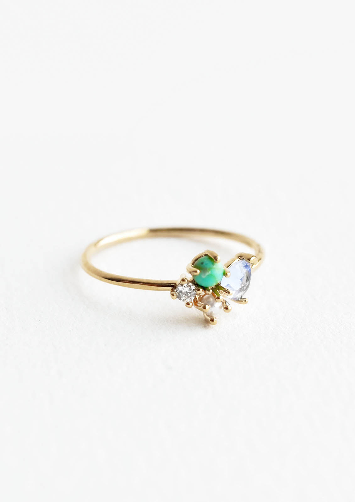 Gold ring featuring slim band with two gemstones and two crystals in blue, green and white hues, prong set in a cluster.