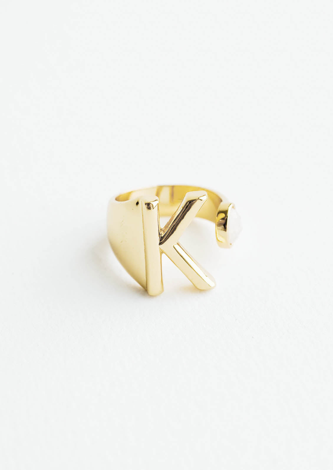 Yellow gold ring with letter K and oval glass crystal, and wide adjustable band.