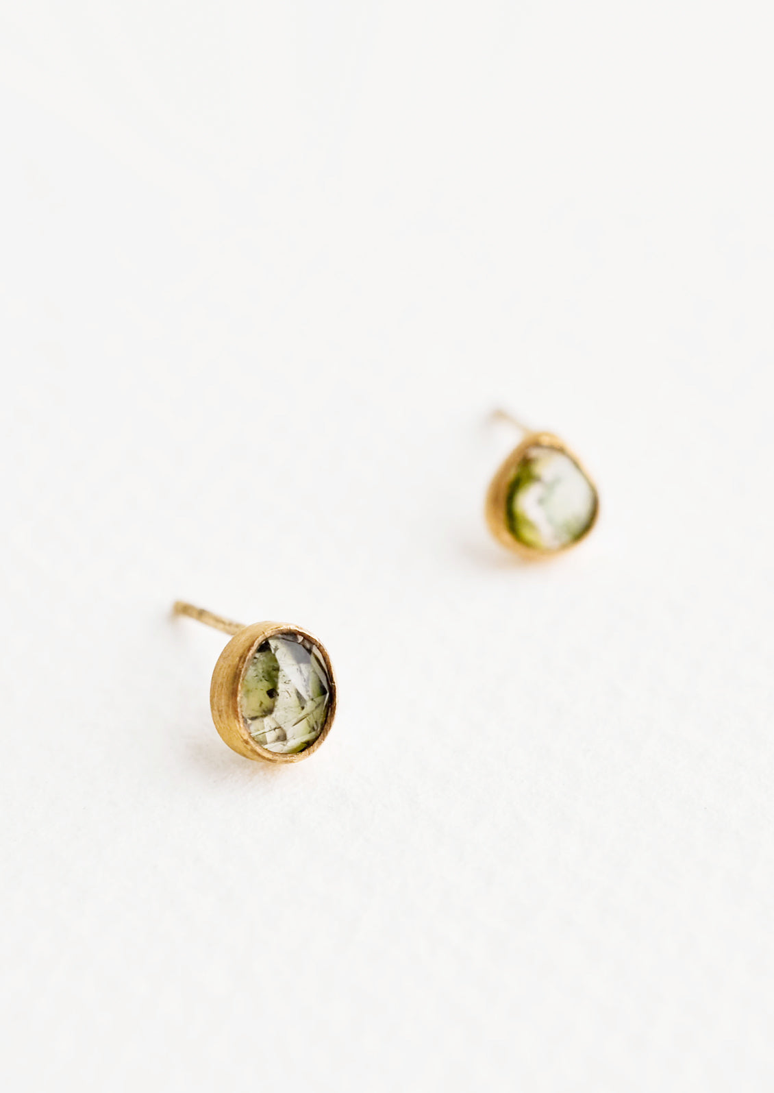 Brass asymmetric stud earrings featuring a green multicolored tourmaline stone.