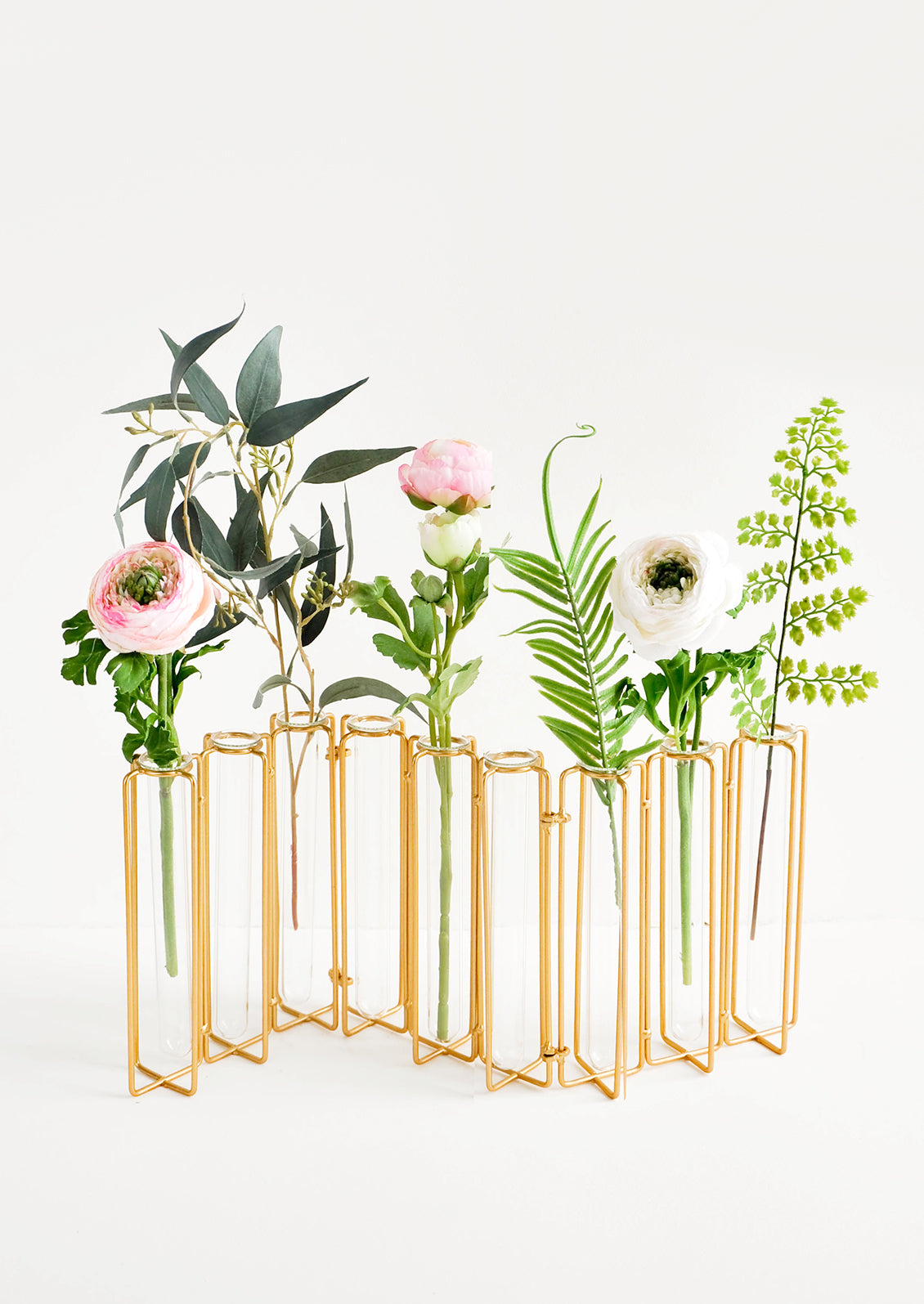 Multi-stem vase composed of nine glass vials side by side, resting inside individual compartments on a brass metal frame.