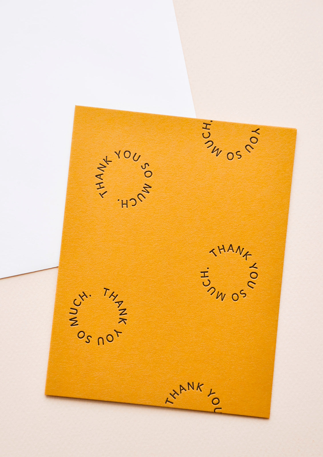 Marigold notecard with the text "Thank you so much" set in a circle several times, with white envelope.