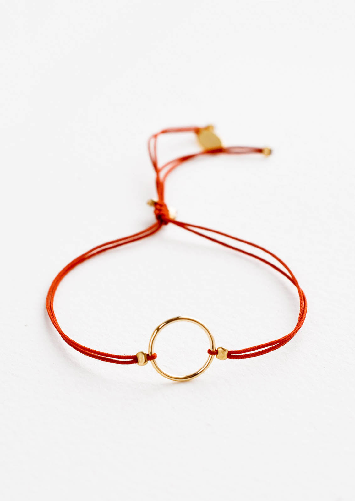 Bracelet with yellow gold circle charm centered on an adjustable red string.