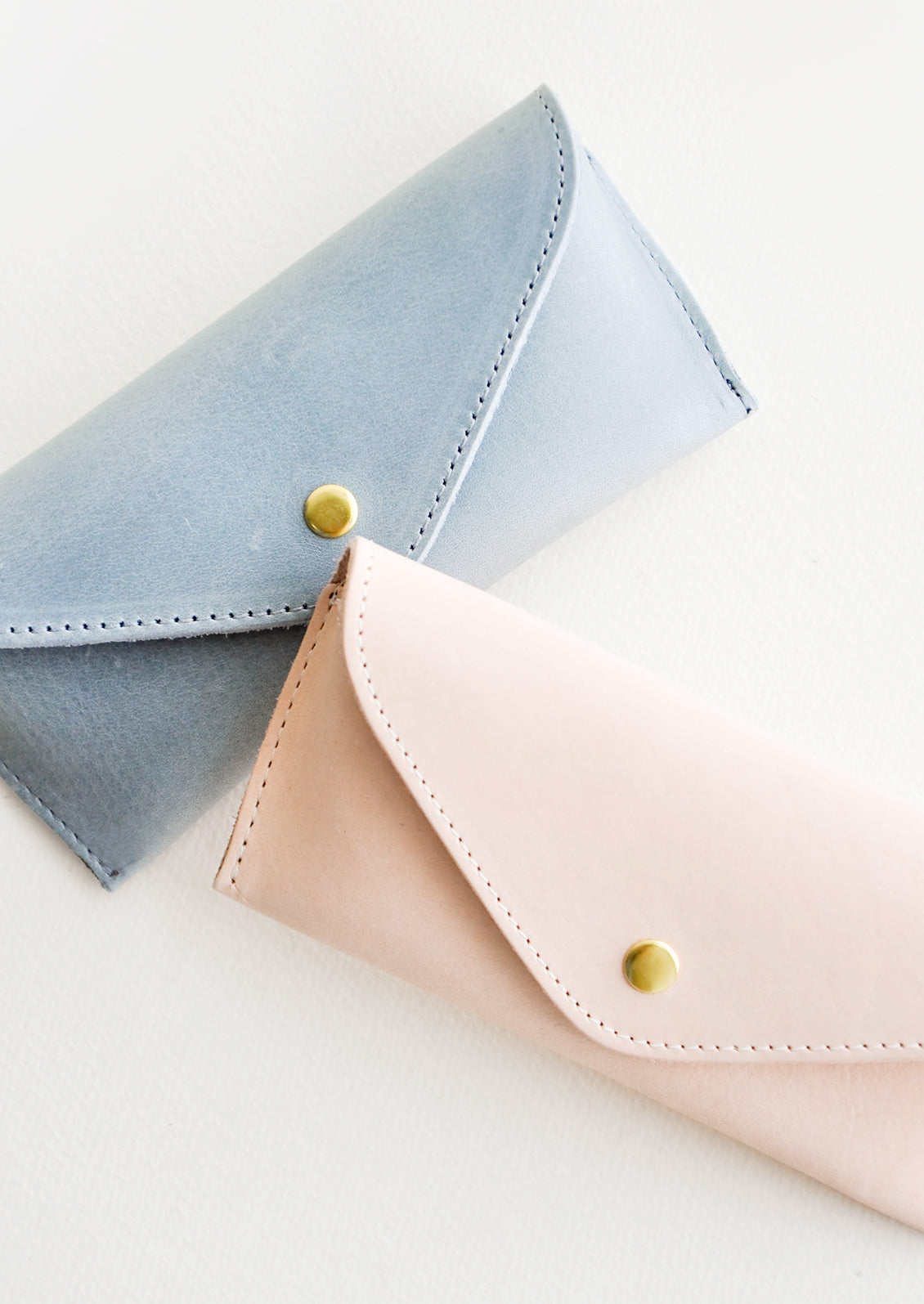 Two leather cases for sunglasses that fold close with a snap, one blue and one pink.