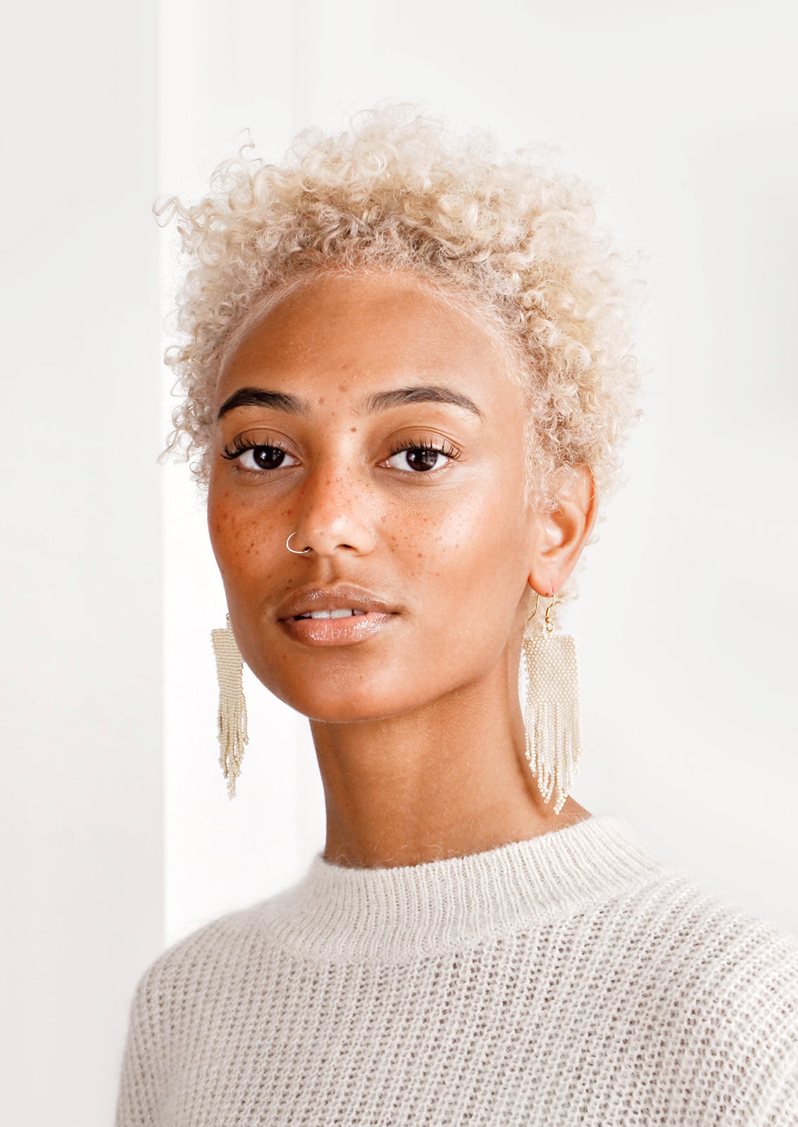 Model wears ivory beaded fringe earrings and white sweater.