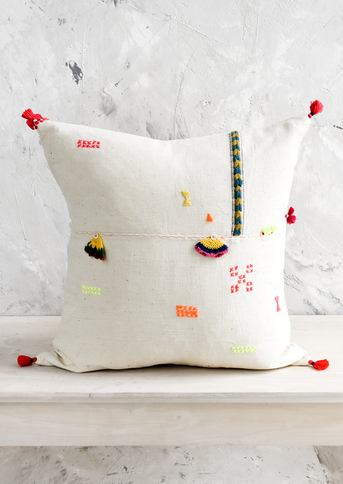 A square throw pillow with neon embroidery and applique detailing.
