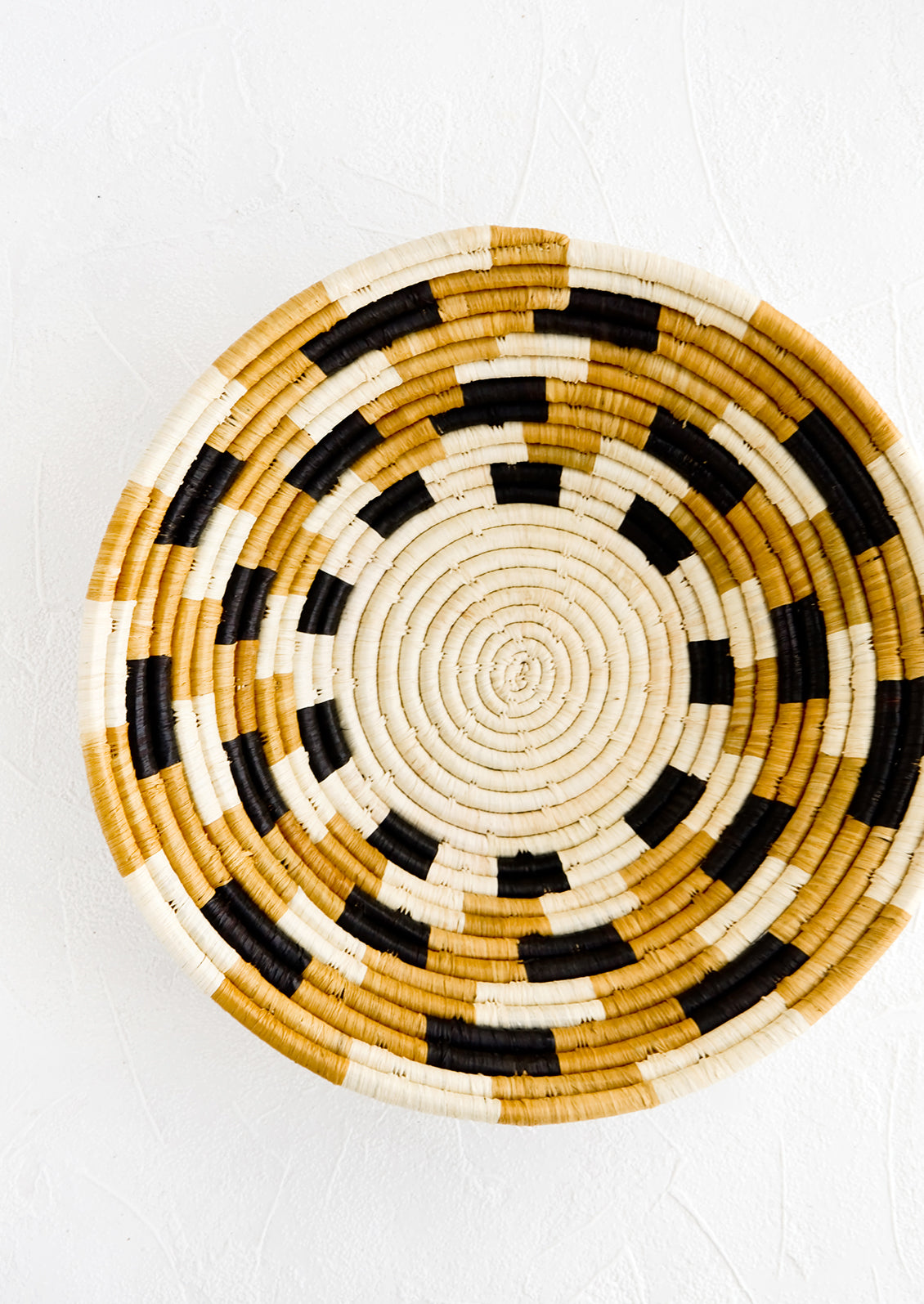 Round woven raffia bowl with checkered pattern in natural, tan and black
