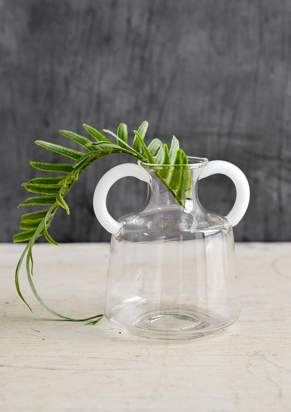 A clear glass vase in short shape with two white handles at top.