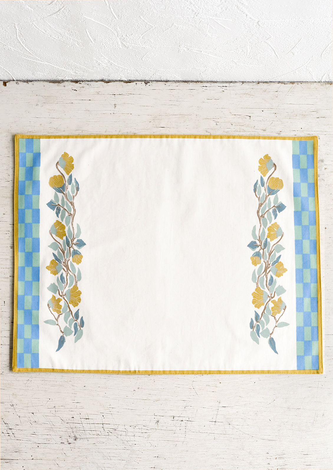 A screenprinted floral placemat with turquoise and blue checker border.