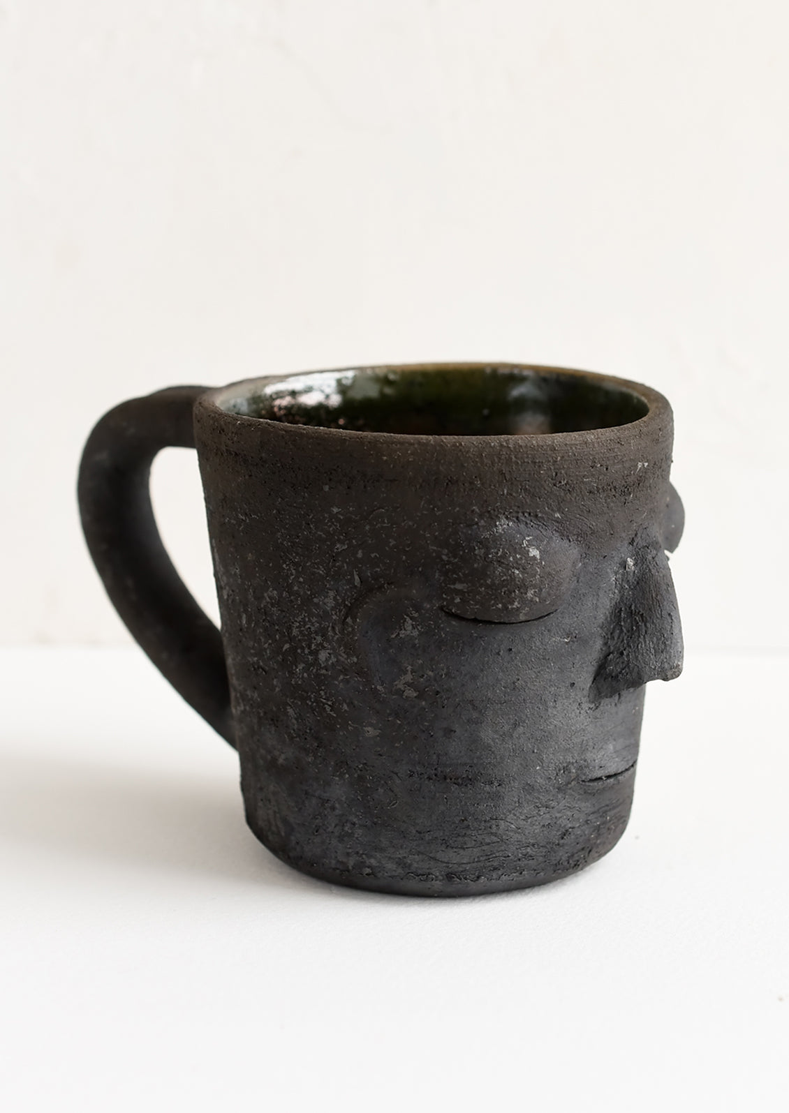 A clay mug in matte black color in face shape.