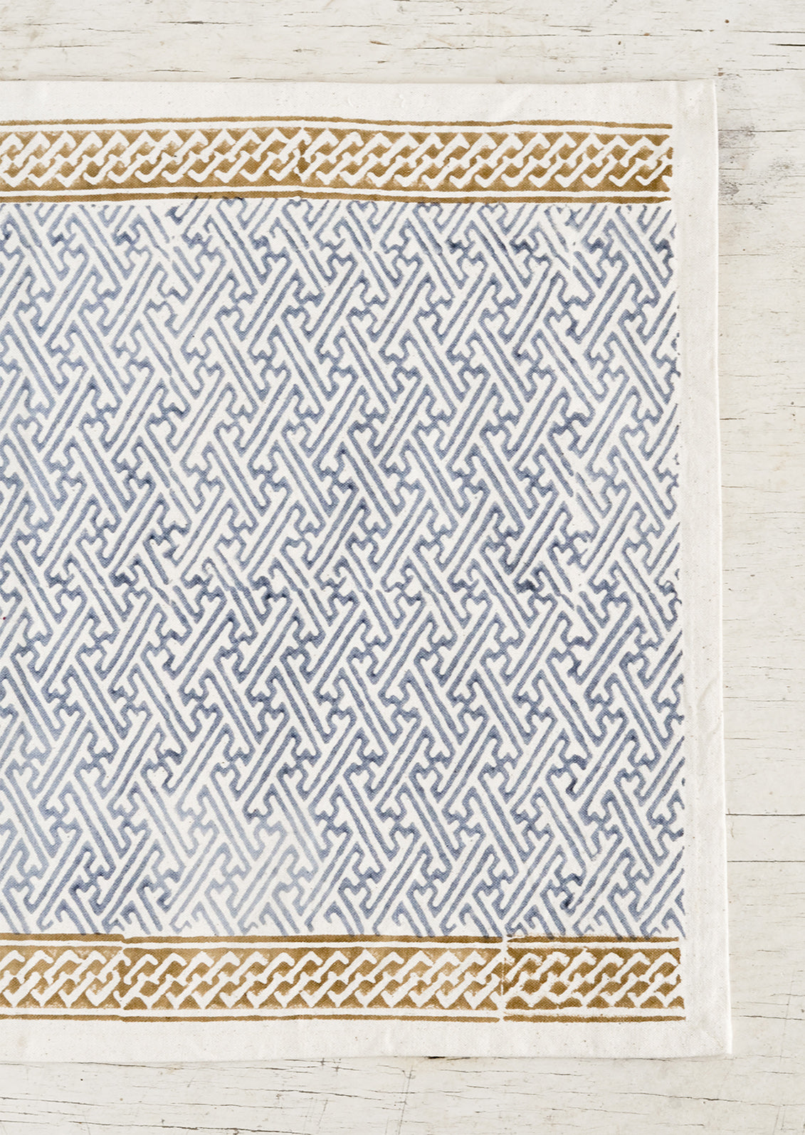 A cotton placemat with block print design, ochre borders at top and bottom with dusty blue maze patterned center.