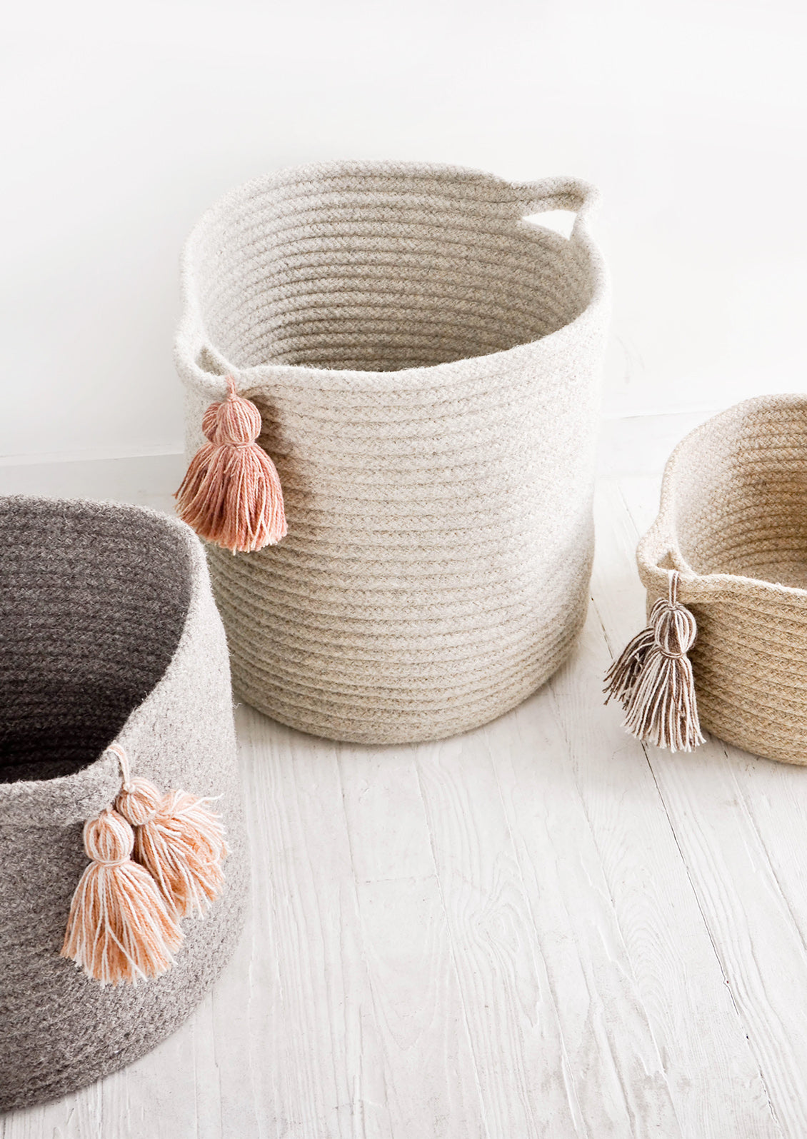 Round storage bins in natural wool. Handles at sides with oversized tassel detail.