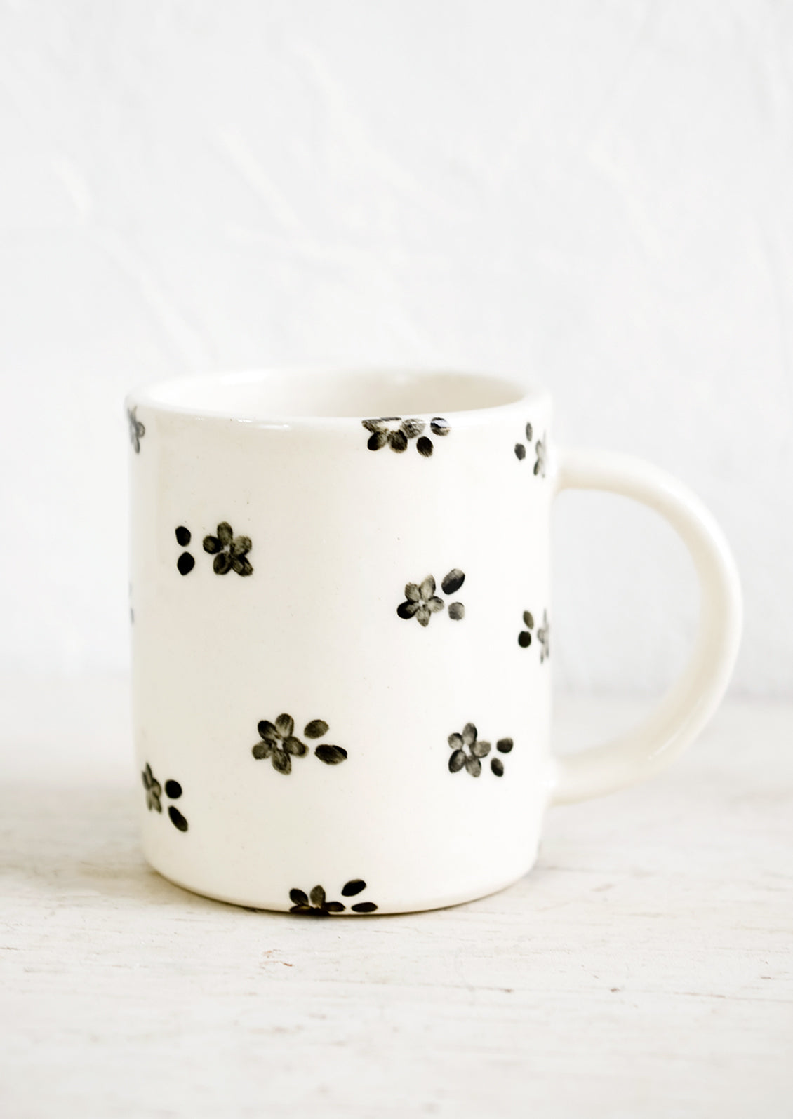 A handmade ceramic mug with white background and hand-painted black floral print.