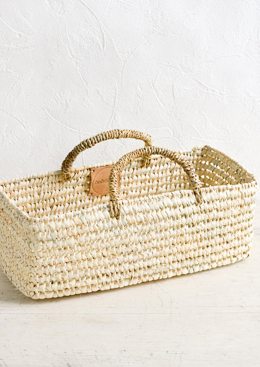 A skinny and narrow square storage basket with handles, made from natural dried palm.