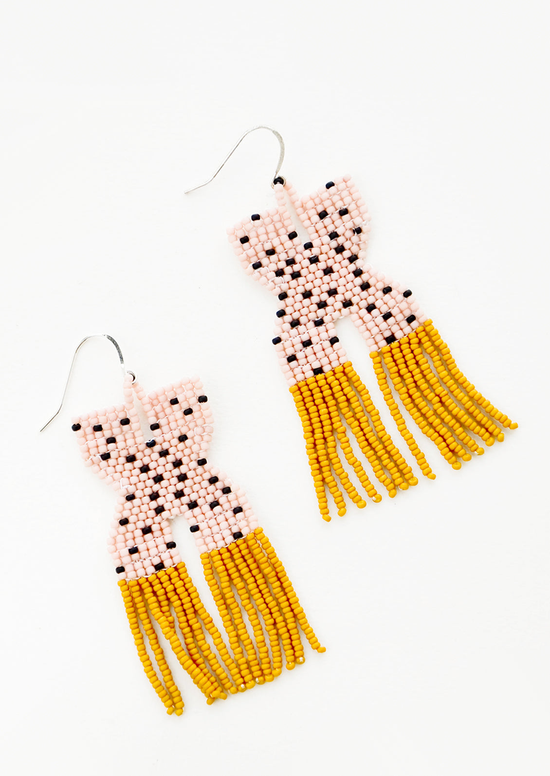 Pink x-shaped beaded earrings with black polka dots and mustard yellow fringe.