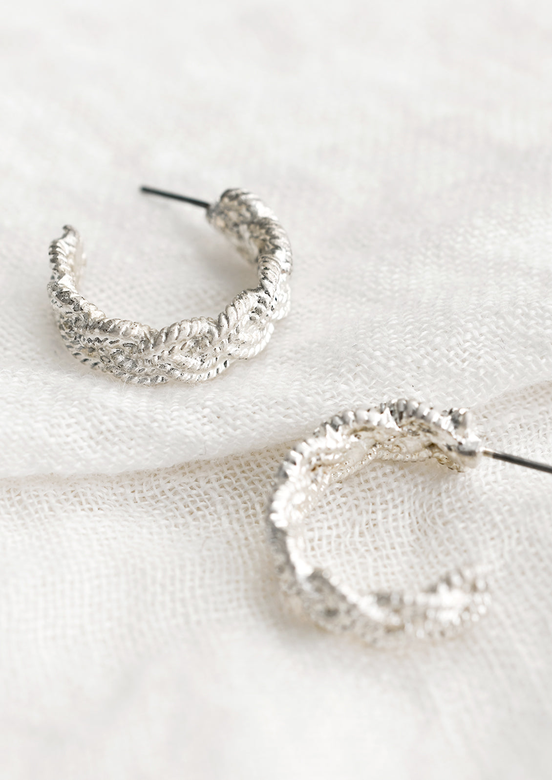 A pair of silver-tone hoop earrings with braided texture.