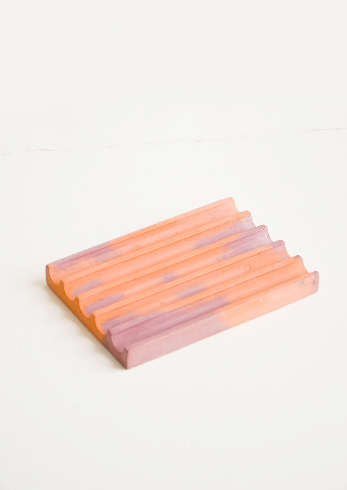 A marbled coral and mauve smooth concrete soap dish with troughs and ridges.