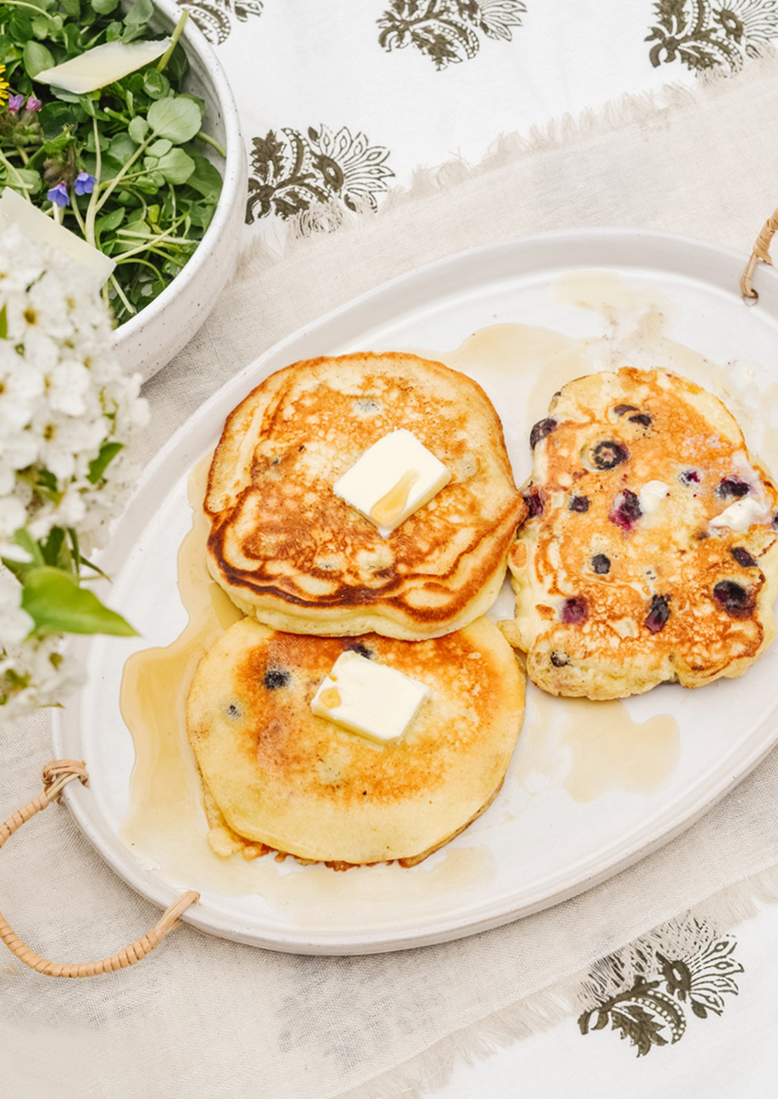A breakfast table setting with pancakes on a ceramic serving platter.