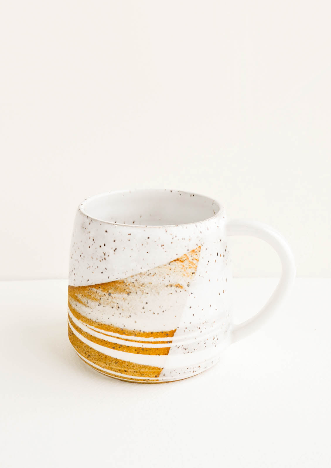 A ceramic mug with a handle in swirled ivory and brown clay with speckled white glazed rim.