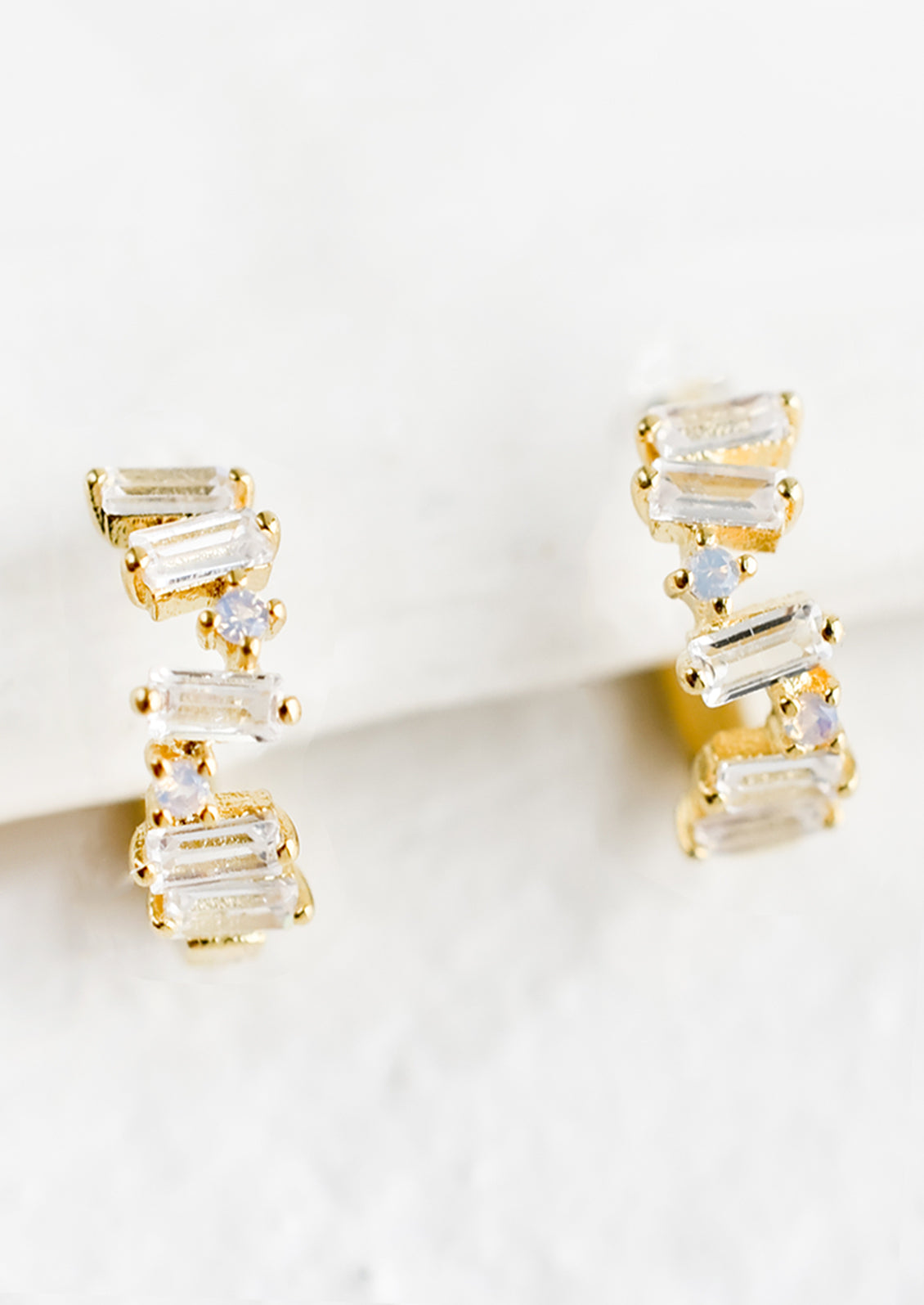 A pair of gold and crystal huggie hoop earrings with clear baguettes.
