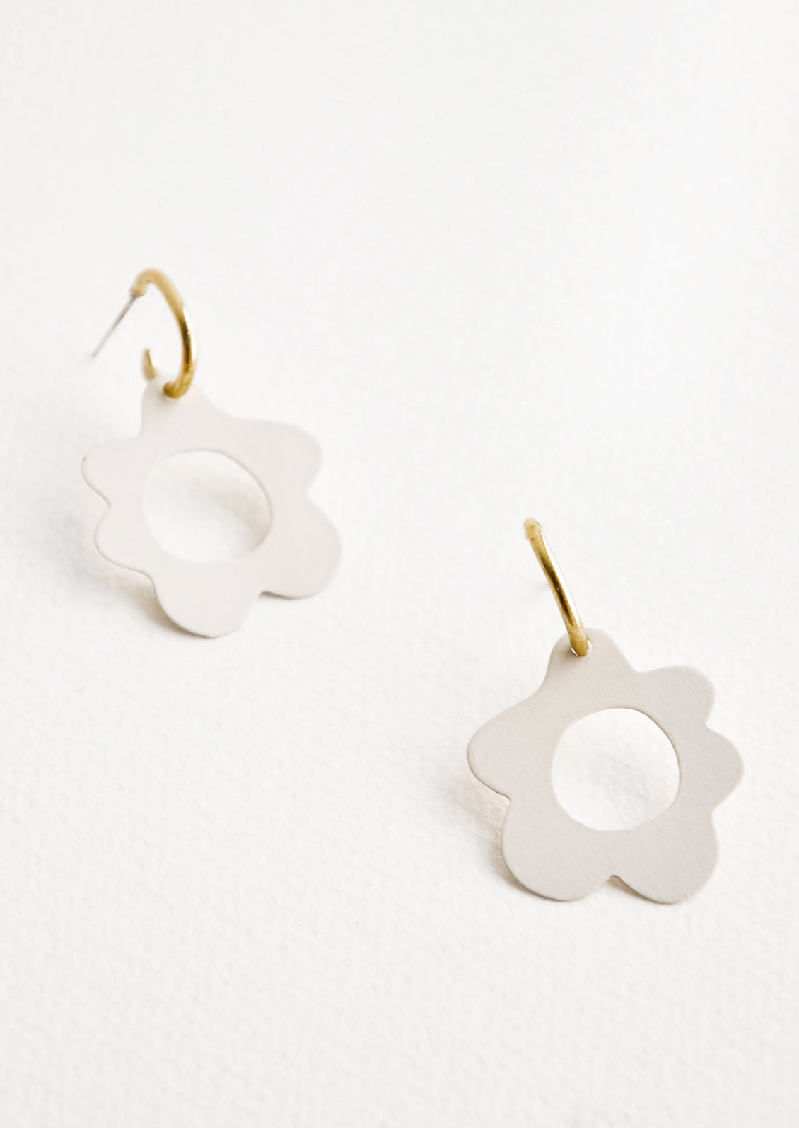 White flower shaped earrings with circular cutouts on small brass open hoops.