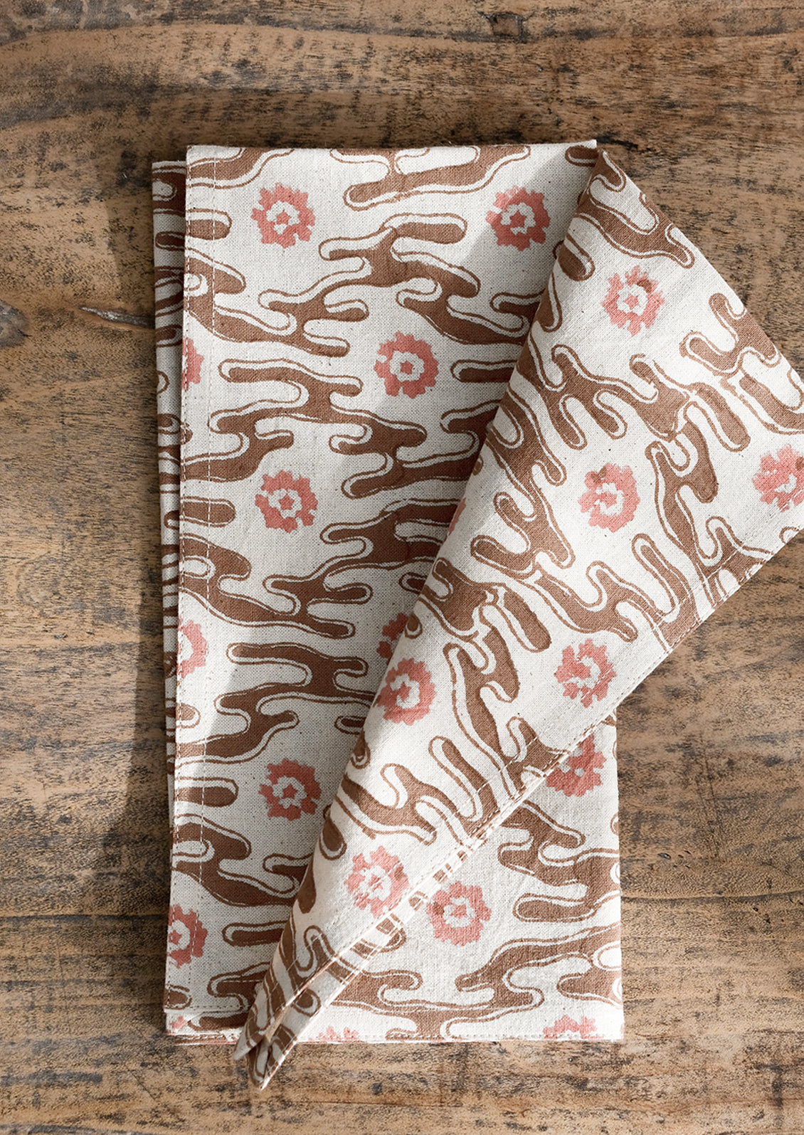 A natural cotton napkin with brown and peach abstract flower print.
