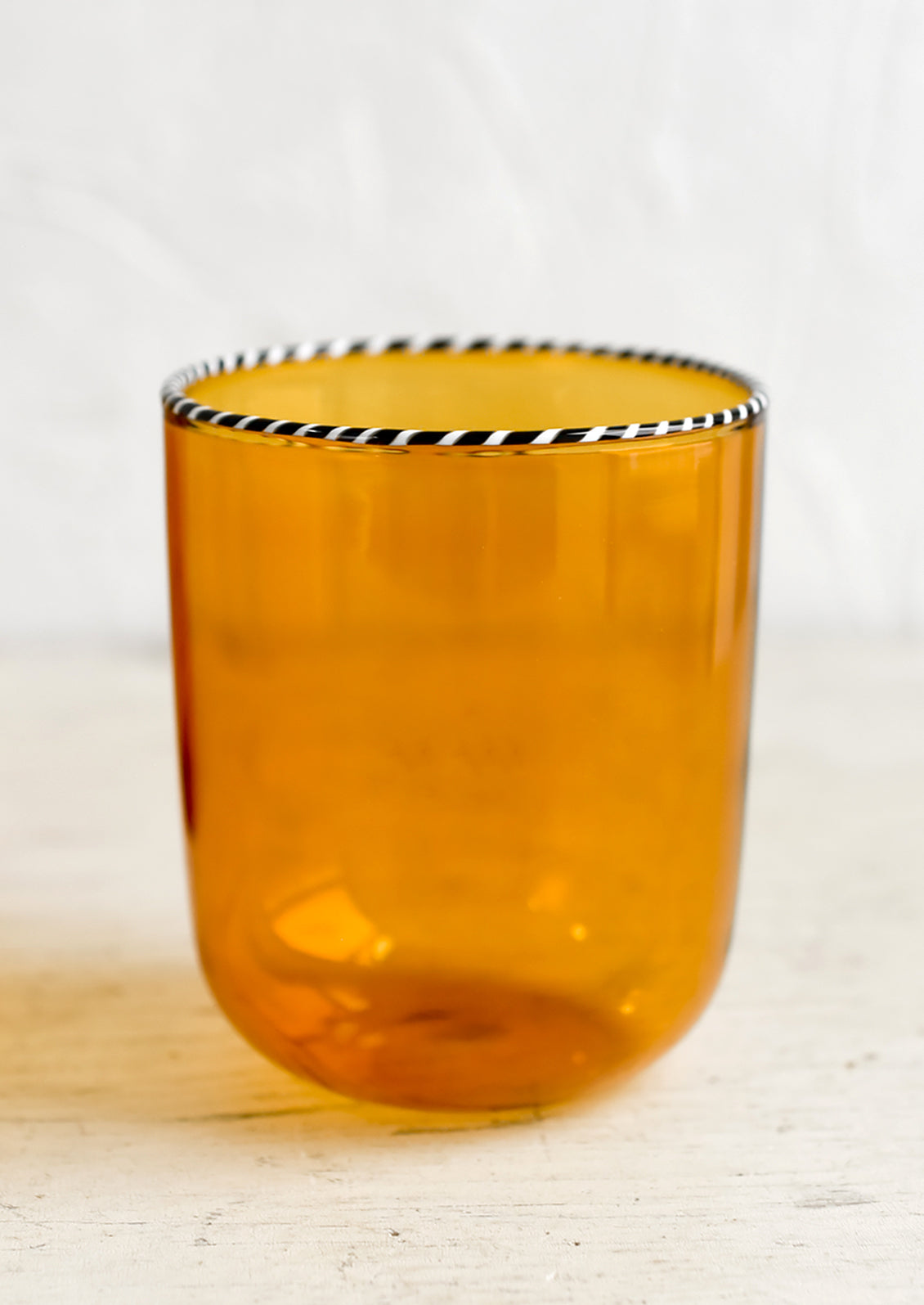 A transparent glass tumbler in amber color with black and white striped rim.