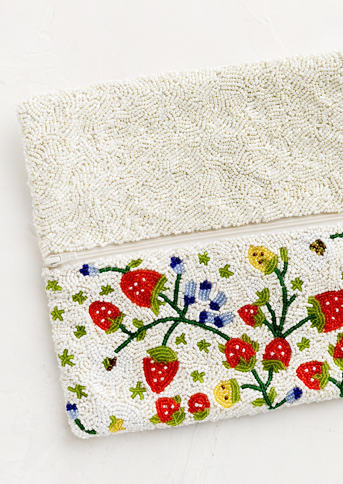 A rectangular foldover beaded clutch in white with multicolor strawberry pattern.