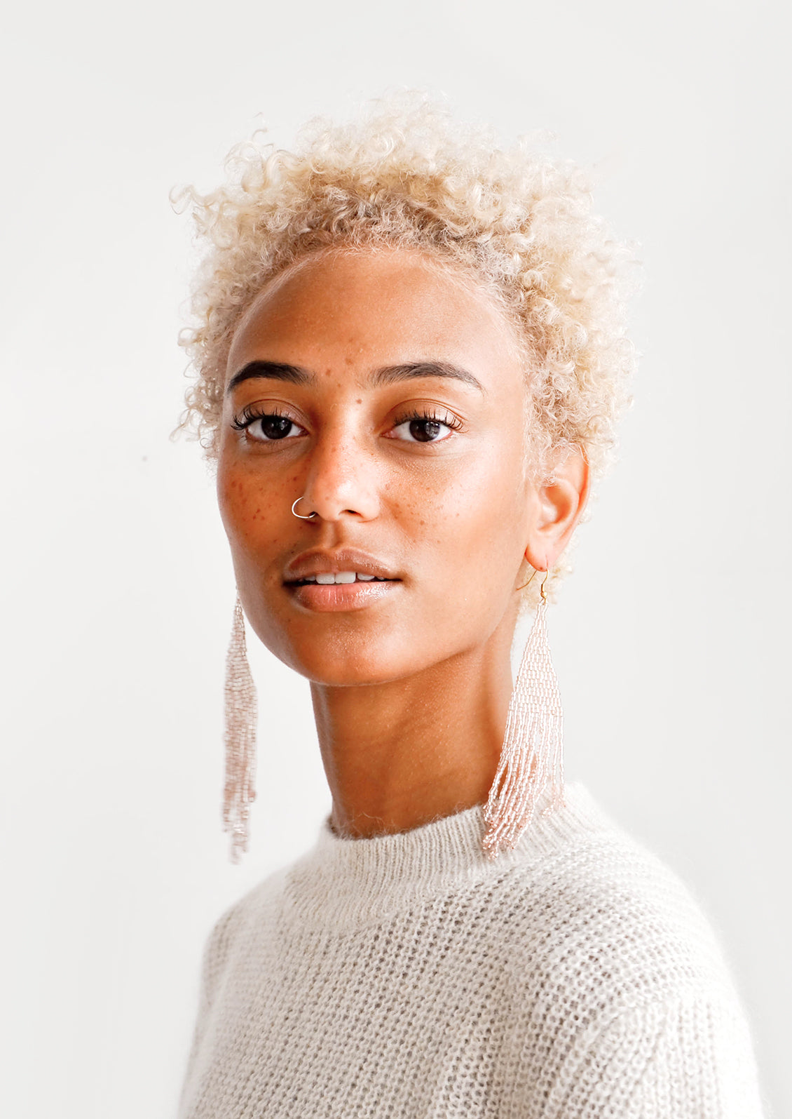 Model wears light pink beaded fringe earrings and white top.