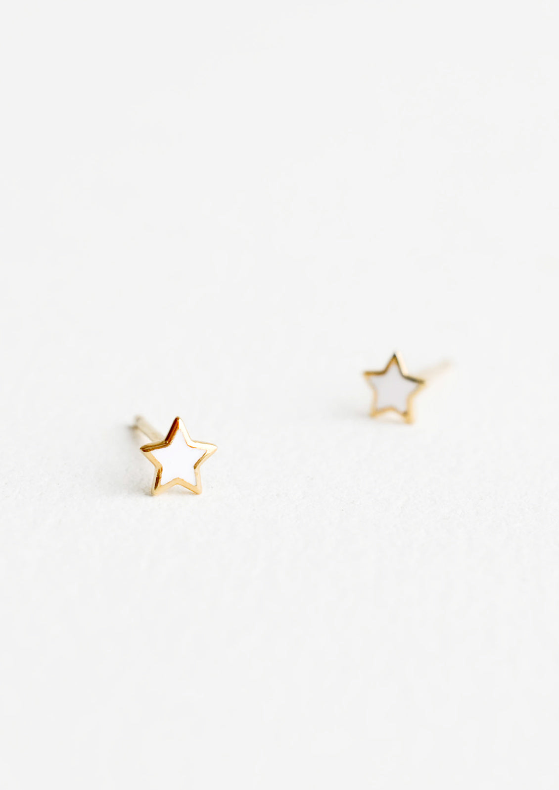 Star shaped stud earrings in white enamel outlined in yellow gold.